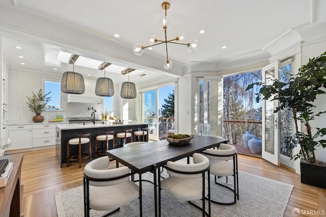 dining room with crown molding, light hardwood / wood-style floors, sink, and a notable chandelier