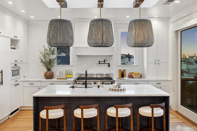 kitchen with oven, an island with sink, and white cabinets