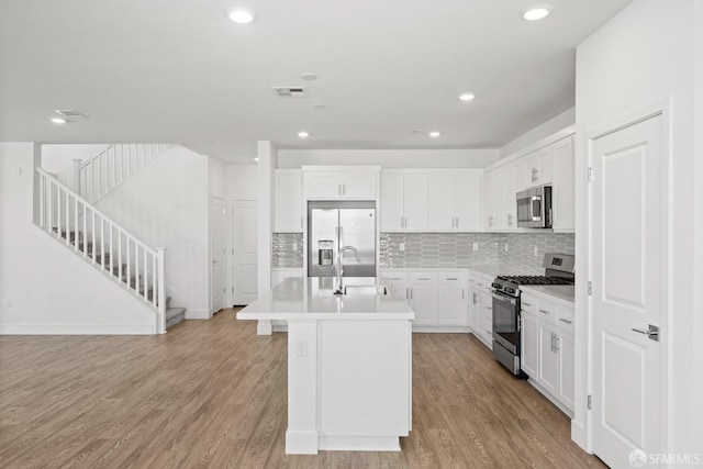 kitchen with stainless steel appliances, an island with sink, white cabinets, and light hardwood / wood-style floors