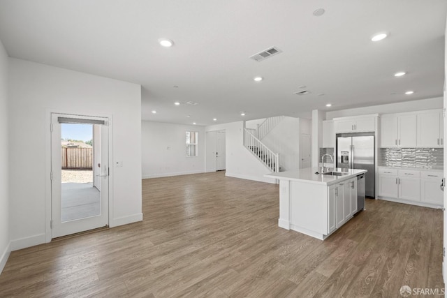 kitchen featuring white cabinetry, a center island with sink, decorative backsplash, and stainless steel fridge with ice dispenser