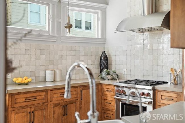 kitchen featuring brown cabinetry, under cabinet range hood, light countertops, high end stainless steel range oven, and decorative backsplash
