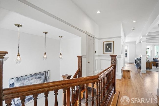 hallway featuring a decorative wall, an upstairs landing, light wood-style floors, recessed lighting, and wainscoting