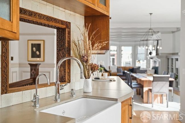 kitchen featuring a notable chandelier, glass insert cabinets, light countertops, brown cabinetry, and a sink