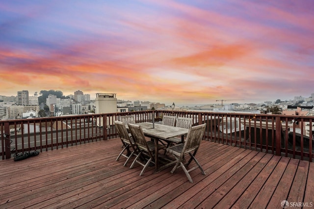deck at dusk featuring outdoor dining space and a city view