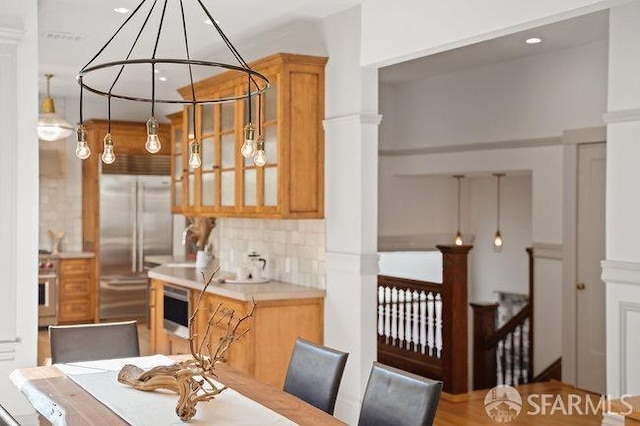 interior space with tasteful backsplash, glass insert cabinets, light countertops, built in fridge, and brown cabinetry