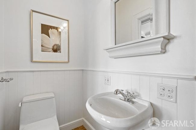half bathroom with toilet, a sink, and wainscoting