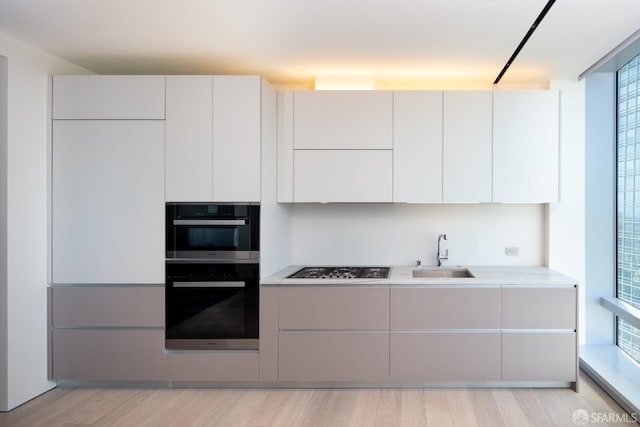 kitchen with white cabinets, light wood-type flooring, stainless steel double oven, gas cooktop, and sink