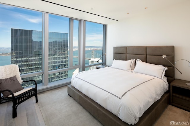 bedroom with floor to ceiling windows, light hardwood / wood-style floors, and a water view