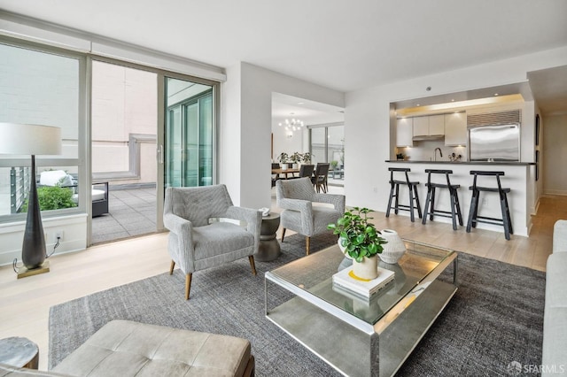 living room featuring an inviting chandelier, light hardwood / wood-style flooring, sink, and a healthy amount of sunlight