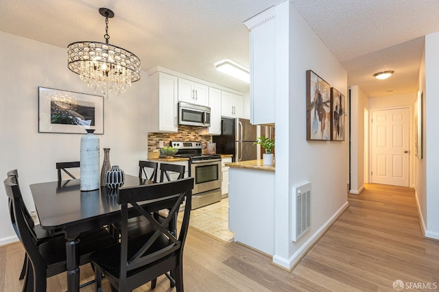 dining area featuring a chandelier, light hardwood / wood-style floors, and a textured ceiling