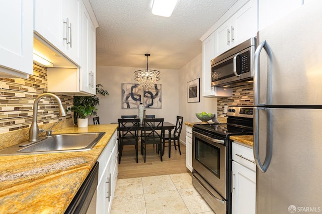 kitchen with stainless steel appliances, sink, white cabinets, and decorative light fixtures