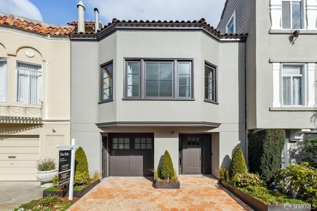 view of front of property with stucco siding, a tiled roof, decorative driveway, and a garage