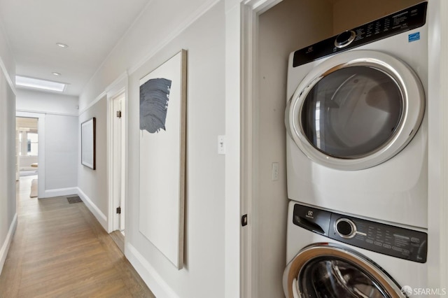 laundry area with light wood-style floors, baseboards, stacked washer and dryer, and laundry area