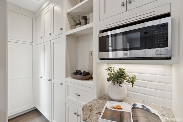 kitchen featuring open shelves, stainless steel microwave, wood finished floors, and white cabinets