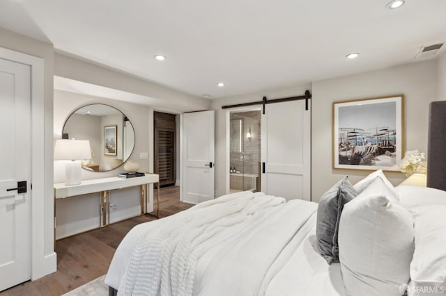 bedroom with visible vents, wood finished floors, recessed lighting, a barn door, and connected bathroom