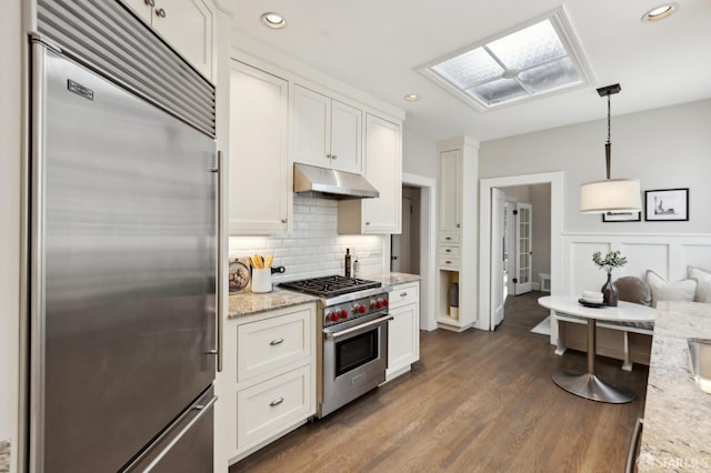 kitchen featuring under cabinet range hood, premium appliances, dark wood-style floors, and white cabinetry