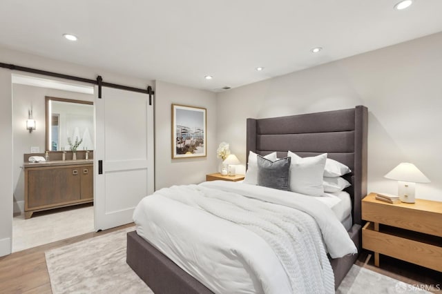 bedroom featuring light wood finished floors, visible vents, recessed lighting, and a barn door