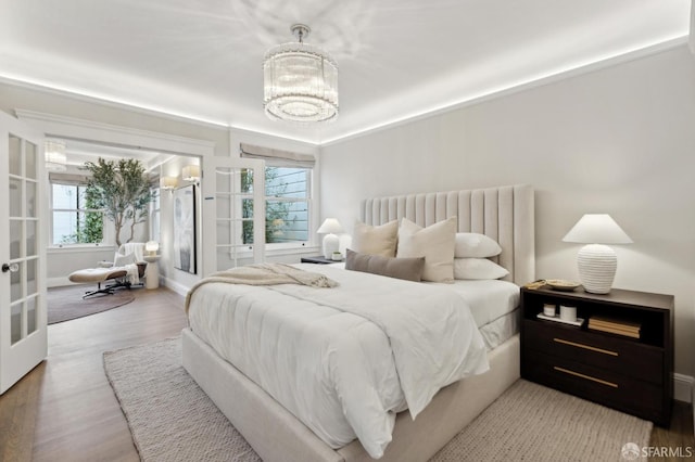 bedroom featuring french doors, multiple windows, a notable chandelier, and wood finished floors