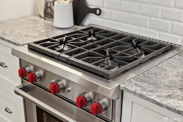 room details with decorative backsplash, white cabinetry, high end stainless steel range oven, and light stone countertops