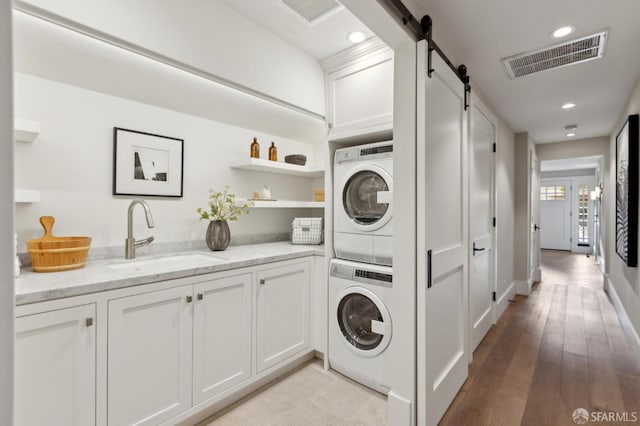 washroom with visible vents, stacked washing maching and dryer, a barn door, and a sink