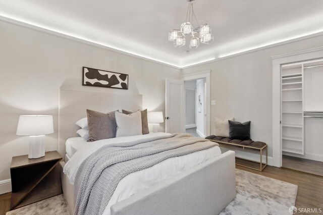 bedroom with a spacious closet, a notable chandelier, wood finished floors, and baseboards