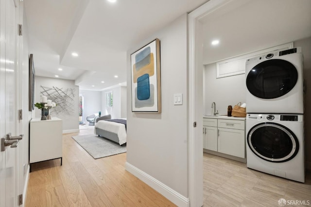 laundry room with light wood-type flooring, stacked washer / drying machine, and sink