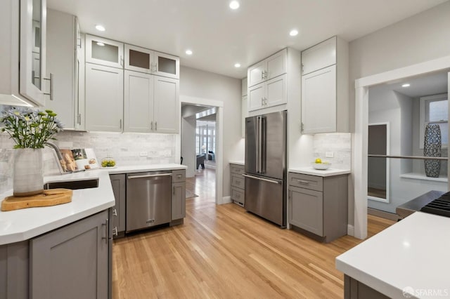 kitchen with gray cabinetry, sink, backsplash, appliances with stainless steel finishes, and light wood-type flooring