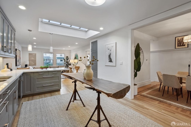 kitchen with gray cabinets, hanging light fixtures, a skylight, light hardwood / wood-style floors, and kitchen peninsula