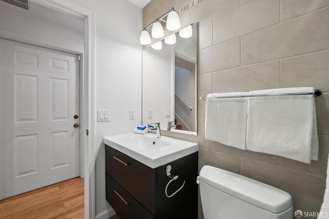 bathroom with vanity, toilet, hardwood / wood-style floors, and tile walls