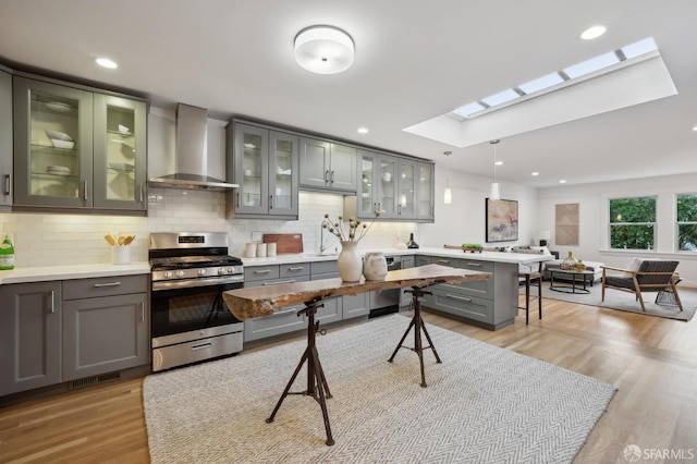 kitchen featuring wall chimney range hood, stainless steel gas range, a breakfast bar area, a skylight, and decorative light fixtures