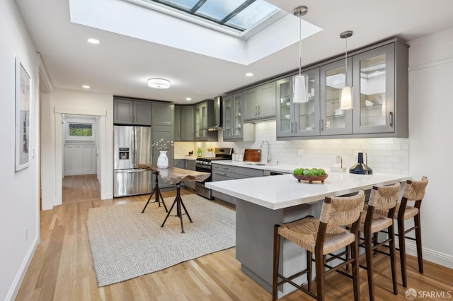 kitchen with appliances with stainless steel finishes, a breakfast bar, pendant lighting, kitchen peninsula, and wall chimney exhaust hood