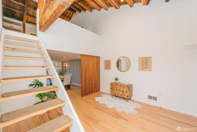 staircase featuring hardwood / wood-style flooring, a high ceiling, and beamed ceiling