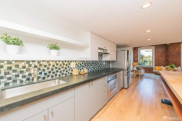 kitchen with sink, white cabinetry, stainless steel appliances, decorative backsplash, and light wood-type flooring