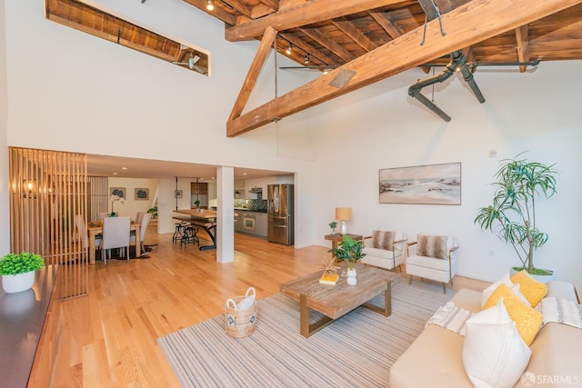 living room with beamed ceiling, a towering ceiling, and light hardwood / wood-style floors