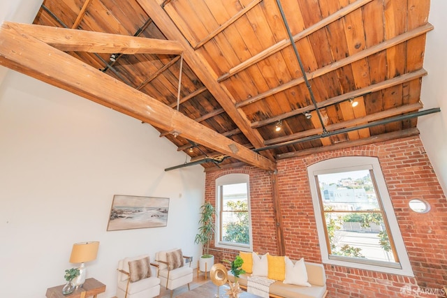 living room featuring beam ceiling, rail lighting, brick wall, and wood ceiling