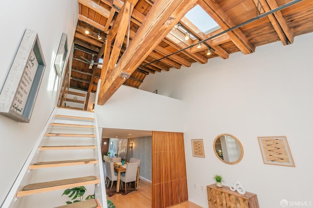 staircase featuring a towering ceiling, hardwood / wood-style floors, wooden ceiling, and beam ceiling