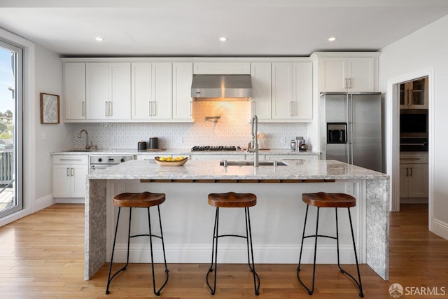 1758 Palou Ave, San Francisco, CA 94124 - kitchen featuring appliances with stainless steel finishes, wall chimney range hood, a kitchen island with sink, decorative backsplash, and a breakfast bar