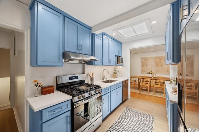67 Rome St, San Francisco, CA 94112 - kitchen with appliances with stainless steel finishes, under cabinet range hood, blue cabinets, light wood finished floors, and light stone counters