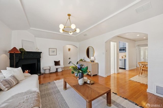 67 Rome St, San Francisco, CA 94112 - living room featuring arched walkways, light wood finished floors, a raised ceiling, and a chandelier