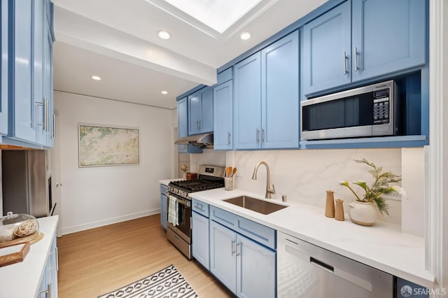 67 Rome St, San Francisco, CA 94112 - kitchen with appliances with stainless steel finishes, blue cabinetry, under cabinet range hood, light wood-style floors, and tasteful backsplash