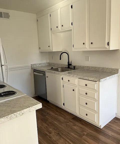 kitchen with light countertops, dark wood-style flooring, stainless steel dishwasher, white cabinetry, and a sink