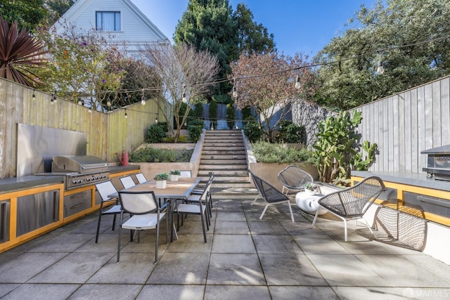 view of patio / terrace with an outdoor kitchen, area for grilling, outdoor dining space, a fenced backyard, and stairs