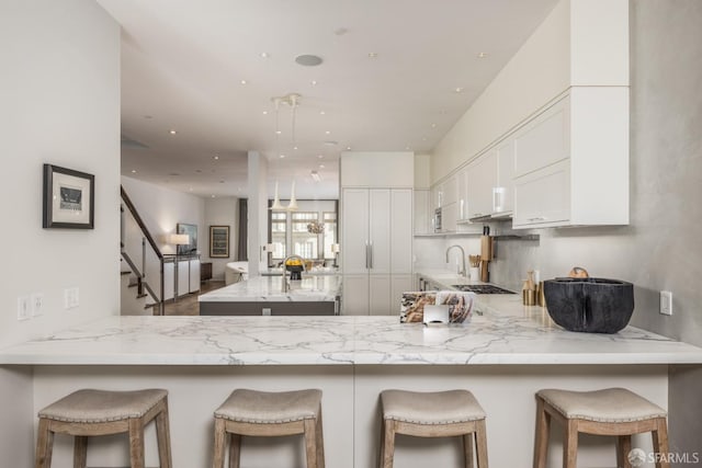 kitchen featuring a peninsula, stainless steel gas stovetop, white cabinetry, a sink, and recessed lighting