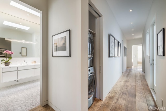 corridor with light wood-style floors, stacked washer / dryer, a sink, and recessed lighting