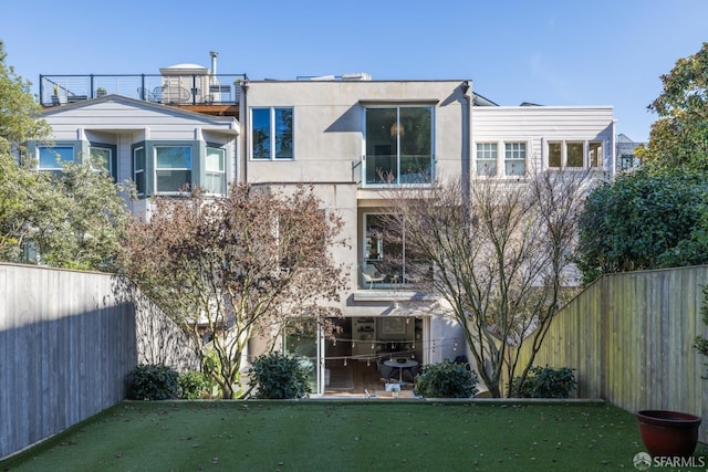 rear view of property featuring a lawn, a fenced backyard, and stucco siding