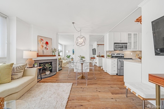 living area featuring a stone fireplace, a notable chandelier, and light wood finished floors