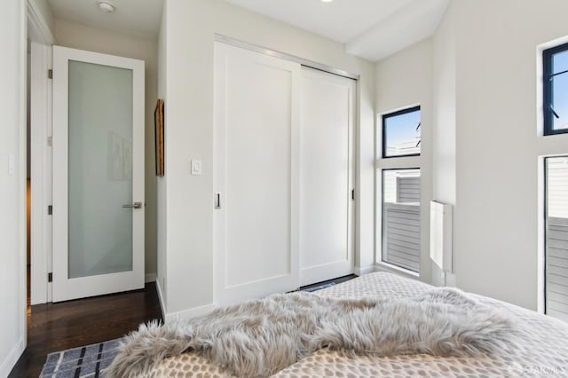 unfurnished bedroom featuring multiple windows, baseboards, dark wood finished floors, and a closet