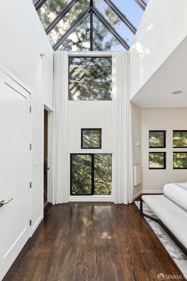 unfurnished living room with dark wood-style floors, a high ceiling, a skylight, and baseboards