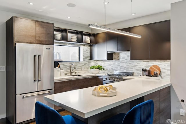 kitchen with premium appliances, dark brown cabinetry, a breakfast bar, a sink, and light countertops