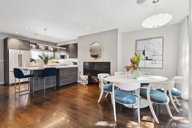 dining space featuring a warm lit fireplace, dark wood-style floors, and recessed lighting